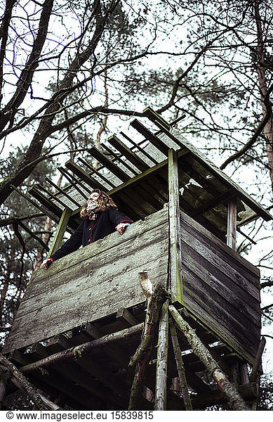 happy young woman smiles and looks out of high tree house look out