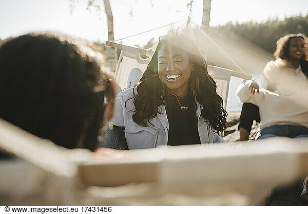 Happy young woman spending leisure time with friends at lakeshore on sunny day