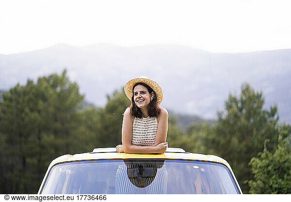 Happy young woman standing in van leaning out from sunroof