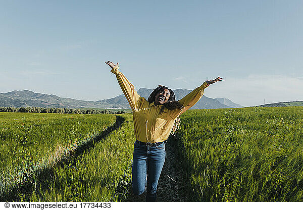 Happy young woman standing with arms raised in meadow
