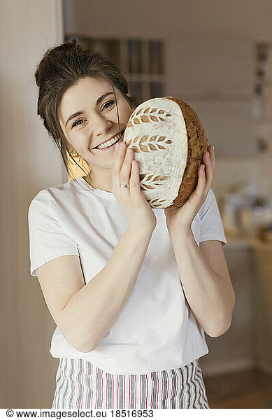 Happy young woman standing with freshly baked bread at home