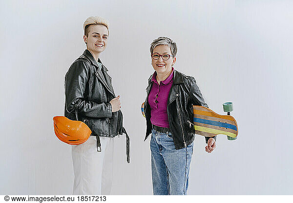 Happy young woman standing with mother holding skateboard in front of white wall