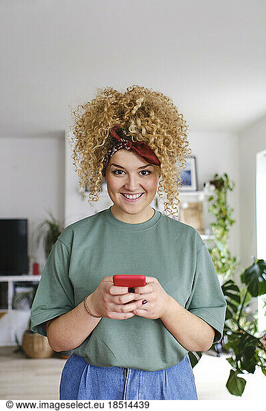 Happy young woman standing with smart phone at home