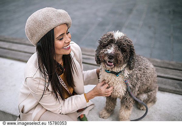 Happy young woman stroking her dog in the city