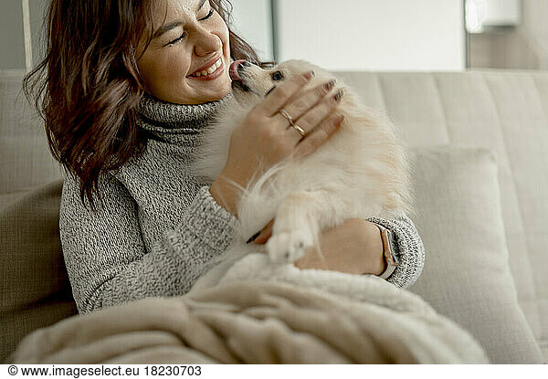 Happy young woman stroking Pomeranian dog at home