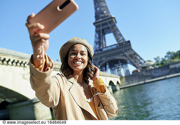 Happy young woman taking selfie through smart phone in front of Eiffel tower  Paris  France
