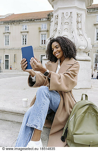 Happy young woman taking selfie through tablet PC sitting on steps