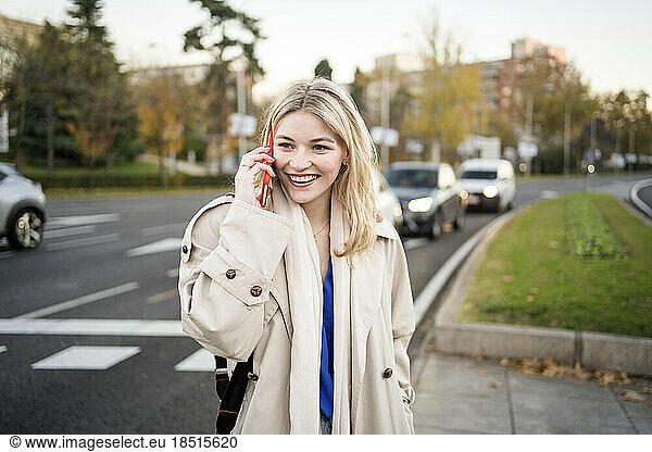 Happy young woman talking on smart phone at roadside