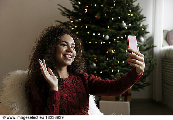 Happy young woman talking on video call waving at smart phone