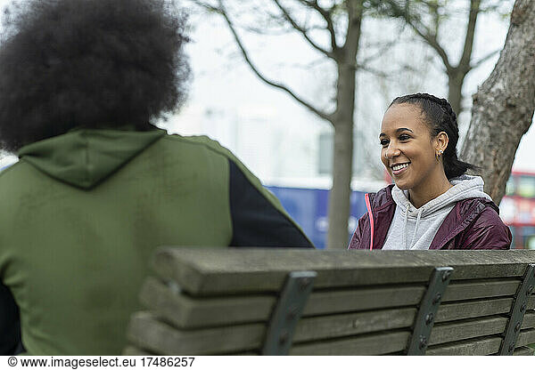 Happy young woman talking with friend on park bench