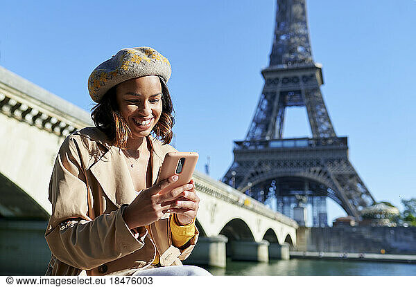 Happy young woman text messaging using smart phone in front of Eiffel tower  Paris  France