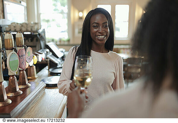 Happy young woman toasting wine glasses with friend in bar