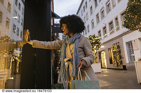 Happy young woman touching glass of store window at footpath