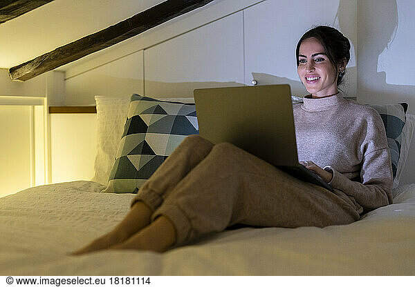 Happy young woman using laptop in bedroom