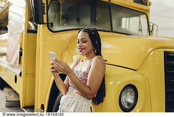 Happy young woman using smart phone leaning on food truck