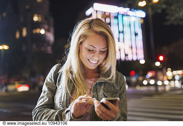 Happy young woman using smart phone on city street at night
