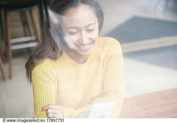 Happy young woman using smart phone sitting at cafe