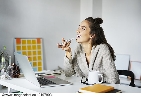 Happy young woman using smartphone at desk