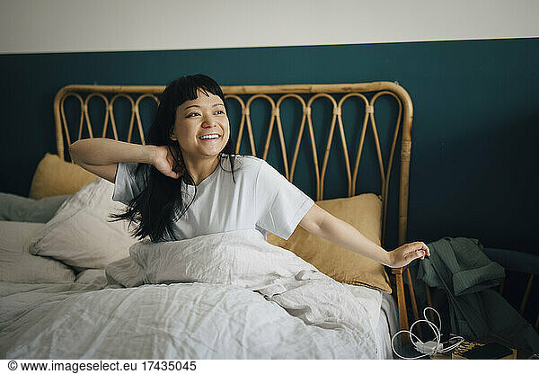 Happy young woman waking up in bed at home