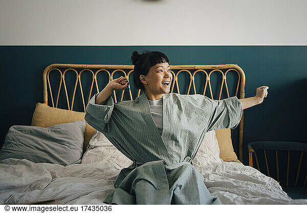 Happy young woman waking up on bed at home