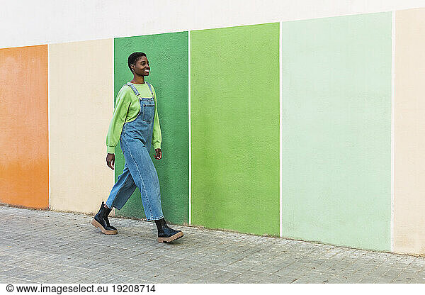 Happy young woman walking in front of multi colored wall at footpath