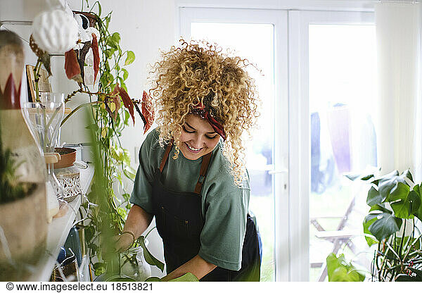 Happy young woman watering plants at home