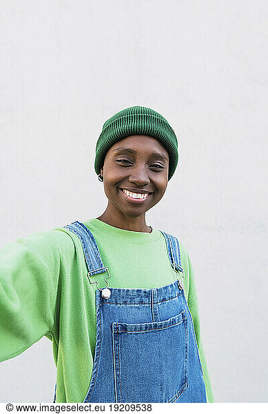 Happy young woman wearing green knit hat in front of white wall