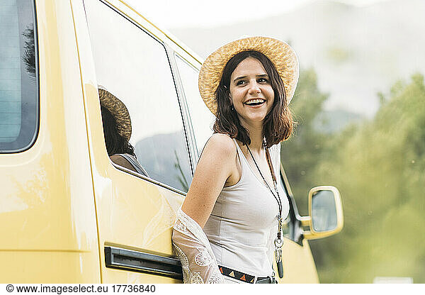Happy young woman wearing hat leaning on van