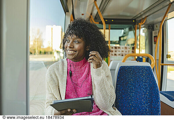 Happy young woman wearing In-ear headphones holding tablet PC in tram