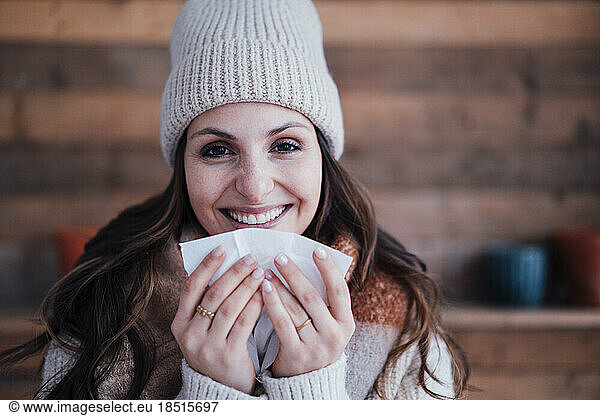 Happy young woman wearing knit hat holding tissue