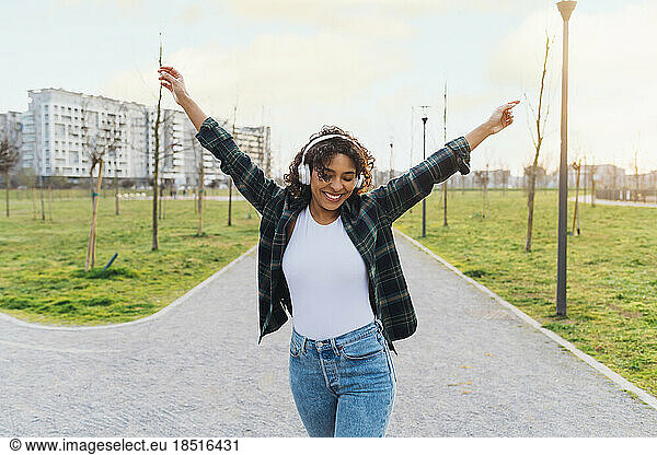 Happy young woman wearing wireless headphones dancing on footpath