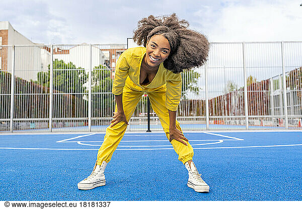Happy young woman with Afro hairstyle bending on sports court