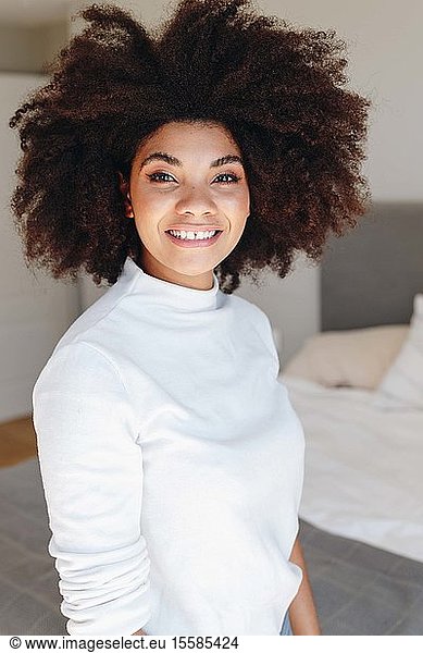 Happy young woman with afro hairstyle in bedroom  waist up portrait
