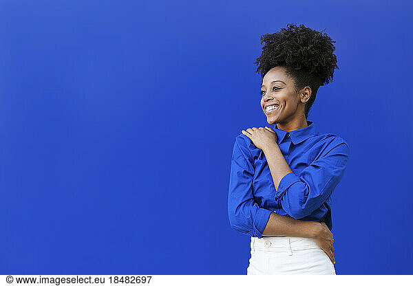 Happy young woman with Afro hairstyle standing over blue background