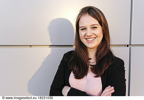 Happy young woman with arms crossed in front of wall