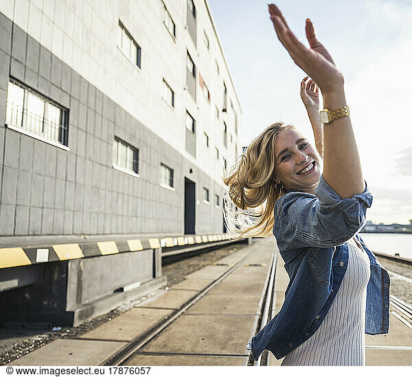 Happy young woman with arms raised dancing in front of building
