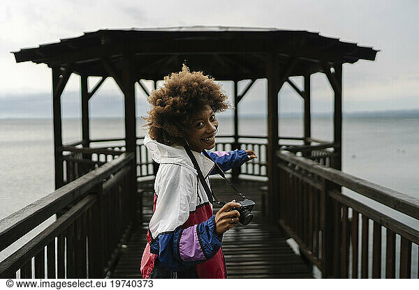 Happy young woman with camera standing in front of gazebo