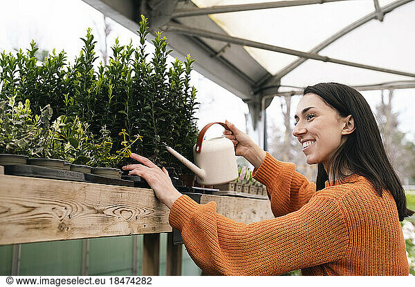 Happy young woman with can watering plants in garden center