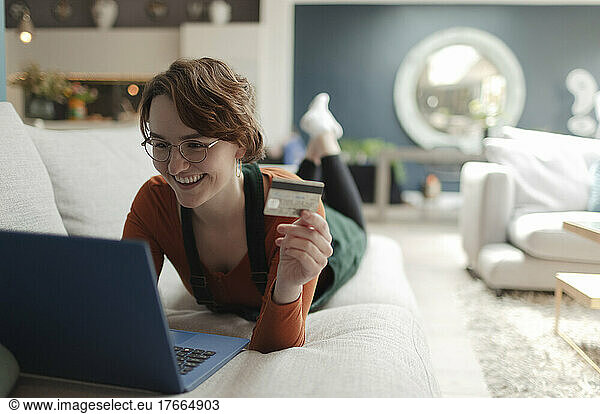 Happy young woman with credit card online shopping at laptop on sofa