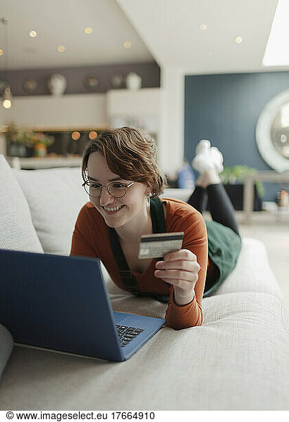Happy young woman with credit card online shopping at laptop on sofa