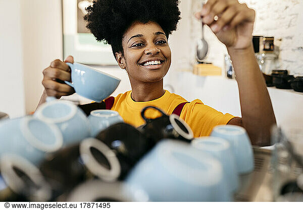 Happy young woman with cup and spoon working in cafe