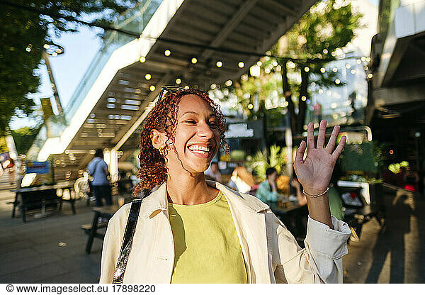 Happy young woman with curly hair waving hand