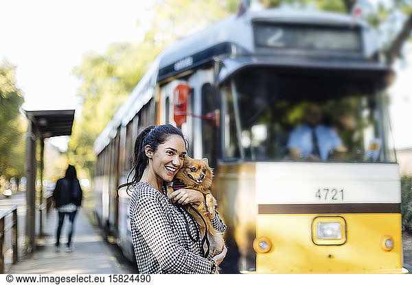 Happy young woman with dog at tram station in the city