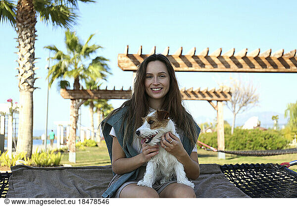 Happy young woman with dog sitting on hammock at park