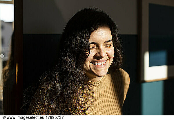 Happy young woman with eyes closed enjoying sunlight at home