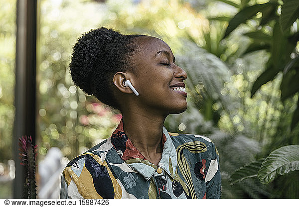 Happy young woman with eyes closed listening music with earphones in garden