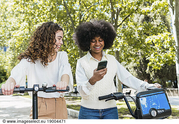 Happy young woman with friend using smart phone in park