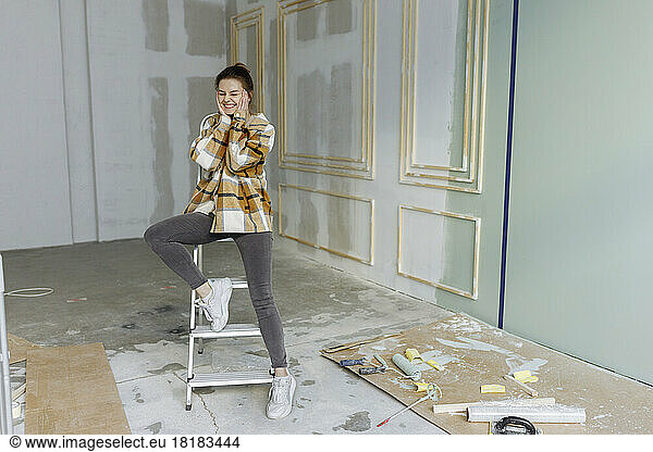 Happy young woman with head in hands leaning on ladder at home