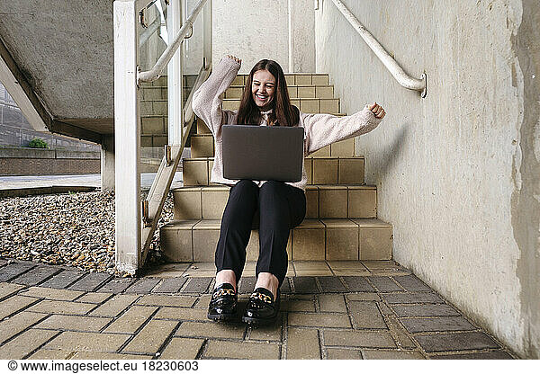 Happy young woman with laptop on staircase