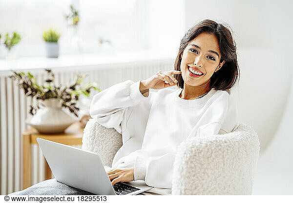 Happy young woman with laptop sitting on chair